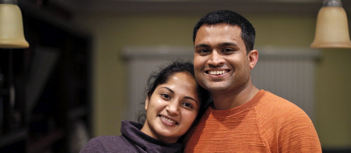 A husband and wife, temporary visa holders stuck in green card backlogs, smile together
