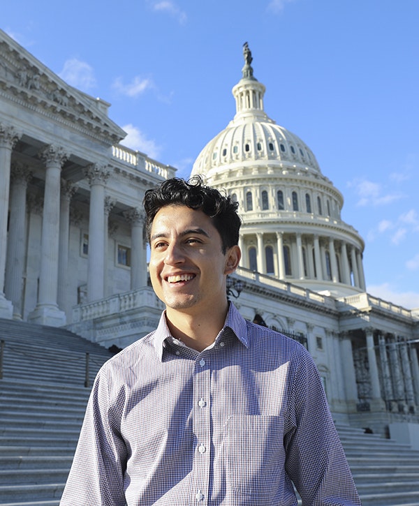 A young man smiles while standing in front of the U.S. Capitol building
