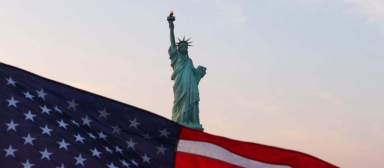 An American flag flies on the back of a boat as the sun sets behind the Statue of Liberty on September 18, 2022, in New York City