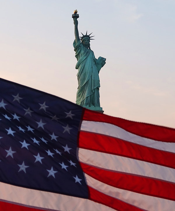 An American flag flies on the back of a boat as the sun sets behind the Statue of Liberty on September 18, 2022, in New York City