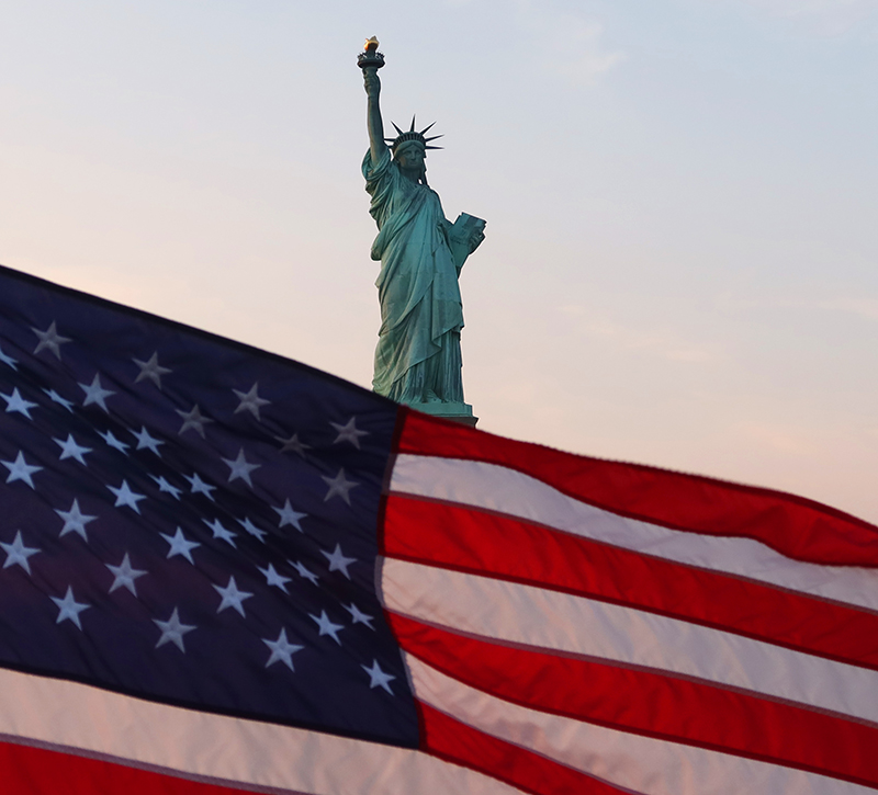 An American flag flies on the back of a boat as the sun sets behind the Statue of Liberty on September 18, 2022, in New York City