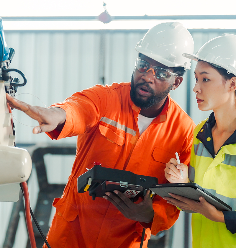 A man and a woman in hard hats and protective gear examine an advanced machine