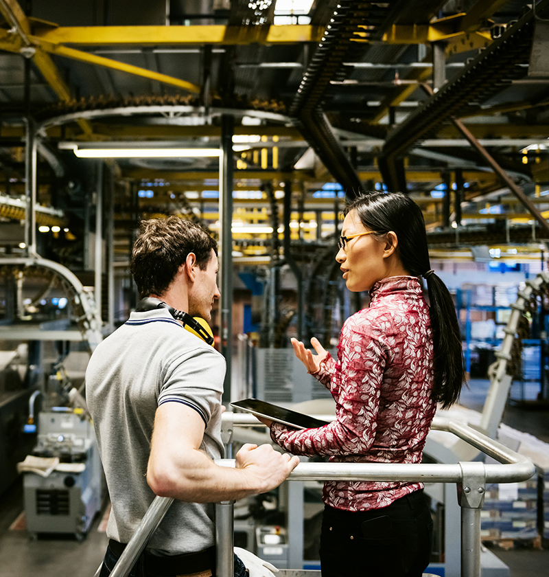 Mechanic and manager talking nearby a machine in a big printery about latest newspaper print