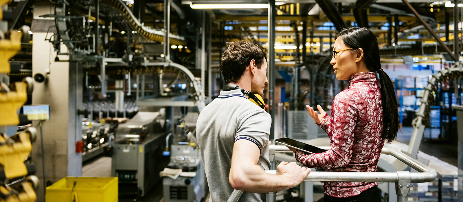 Mechanic and manager talking nearby a machine in a big printery about latest newspaper print