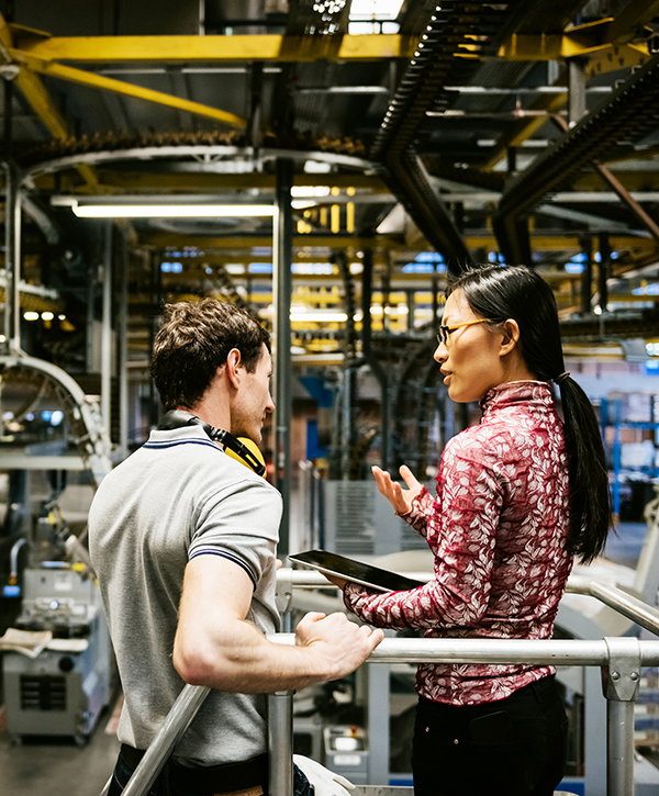 Mechanic and manager talking nearby a machine in a big printery about latest newspaper print