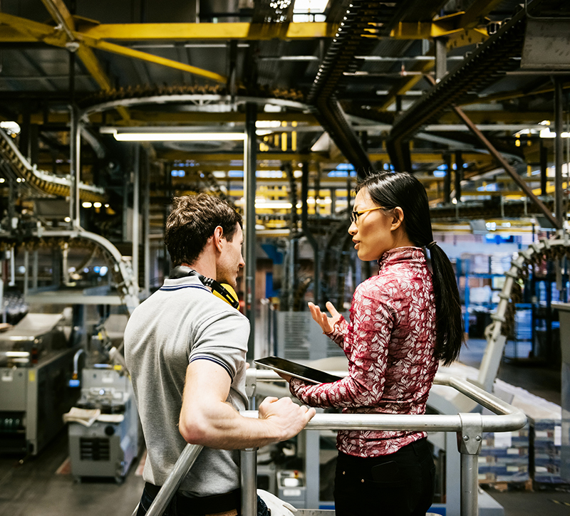 Mechanic and manager talking nearby a machine in a big printery about latest newspaper print