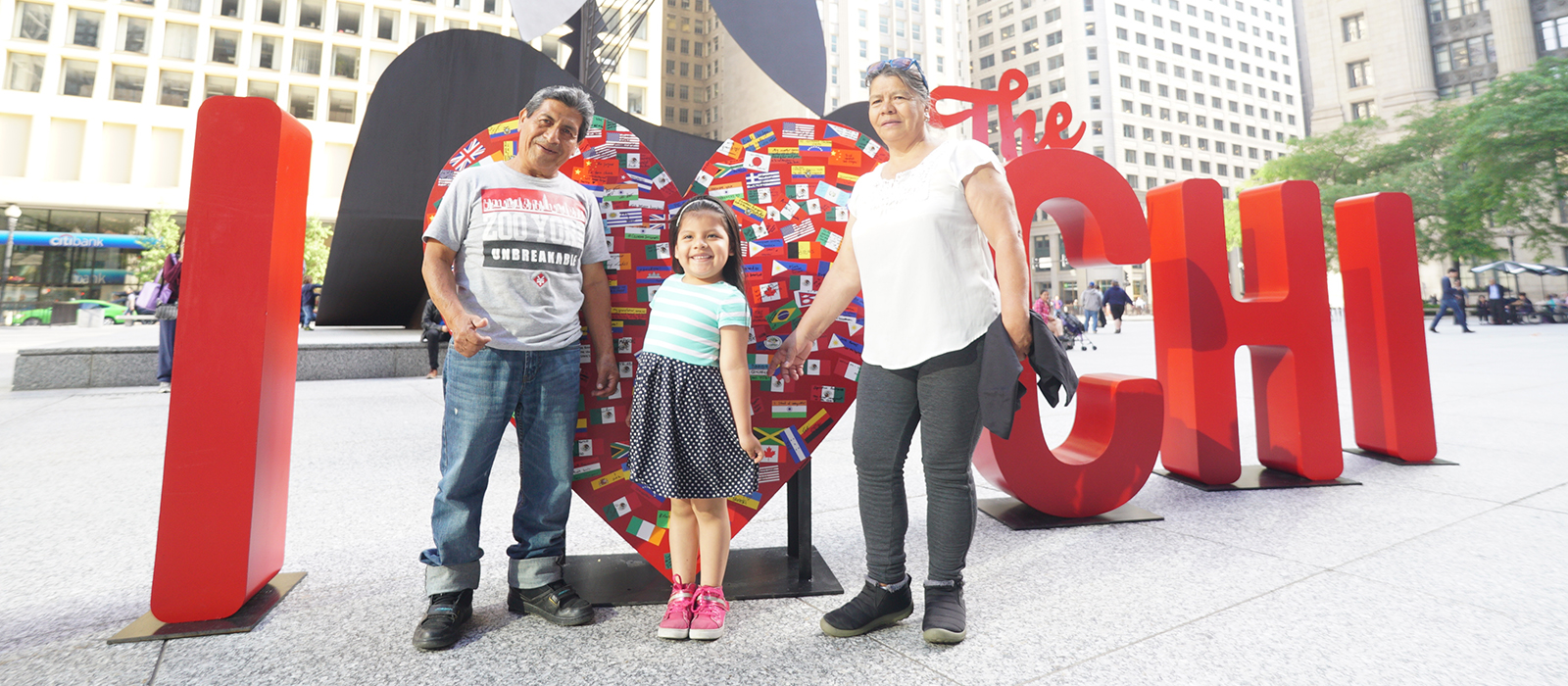 A family poses in front of an "I Heart the Chi" art installation during Immigrant Heritage Month in June